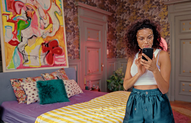 : Femeie cu părul &icirc;nchis folosind Philips Lumea pentru a &icirc;ndepărta părul facial &icirc;n timp ce privește &icirc;n oglinda din baie.