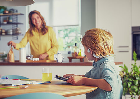 Băiat urmărind videoclipuri &icirc;n timp ce utilizează căştile wireless Philips cu design deschis pentru copii