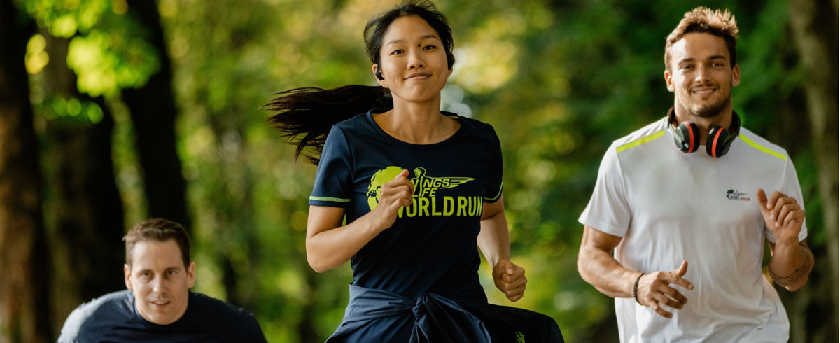 Trei participanţi la Wings for Life World Run aleargă cu bucurie, purt&acirc;nd căşti sport Philips.