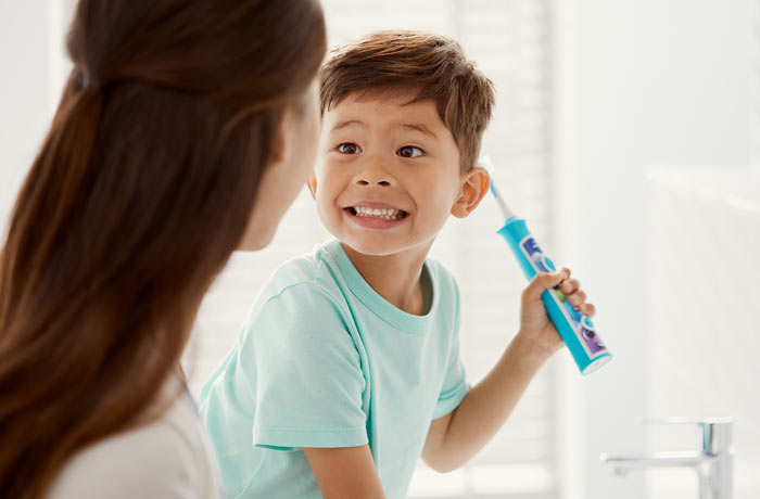 Un băiețel z&acirc;mbește larg spre mama lui, &icirc;n timp ce ține o periuță de dinți Philips Sonicare pentru copii. 